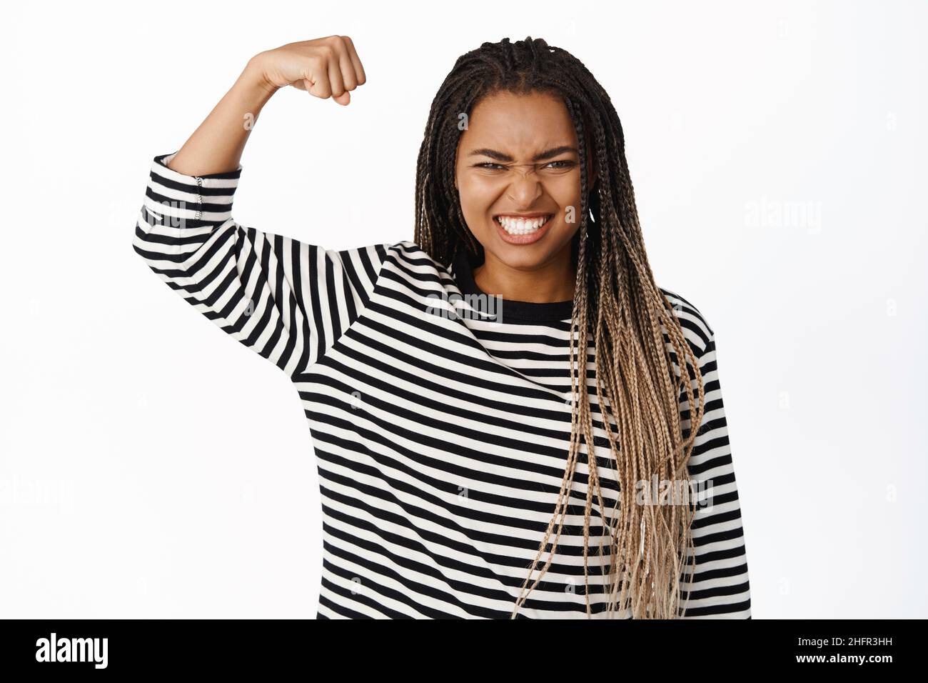 Women power and strength. Sassy black girl showing her muscles, flexing biceps on arm and clench teeth, making power pose, being strong and powerful Stock Photo
