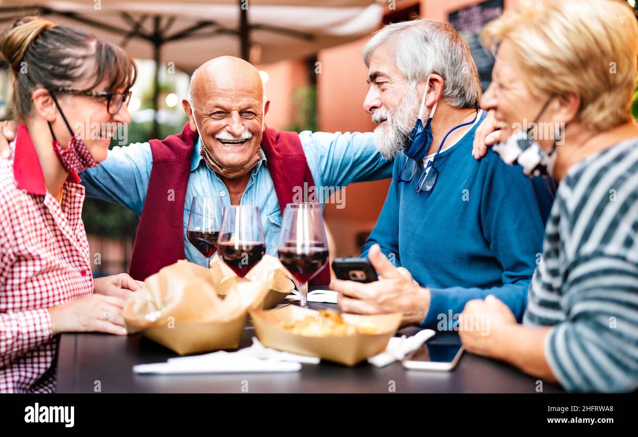 Adult friends drinking wine at restaurant bar wearing open face masks - New normal life style concept with happy mature couples having fun together Stock Photo