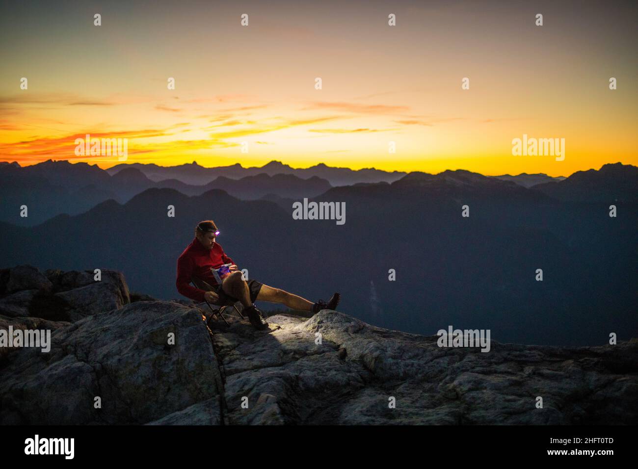 Hiker sitting on mountain summit, enjoying the sunrise. Stock Photo