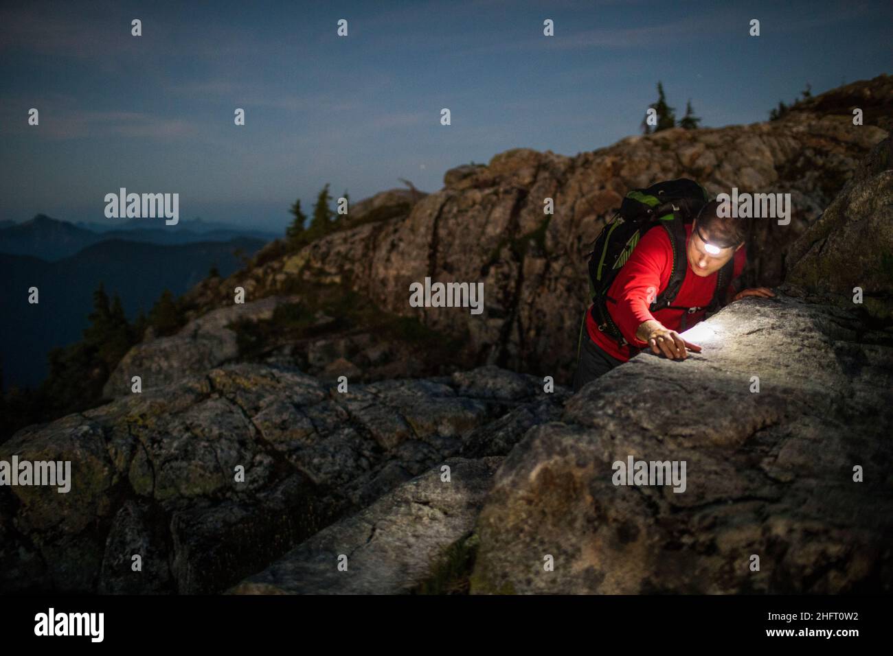 Mountain climber navigates a large boulder at night with headlamp on