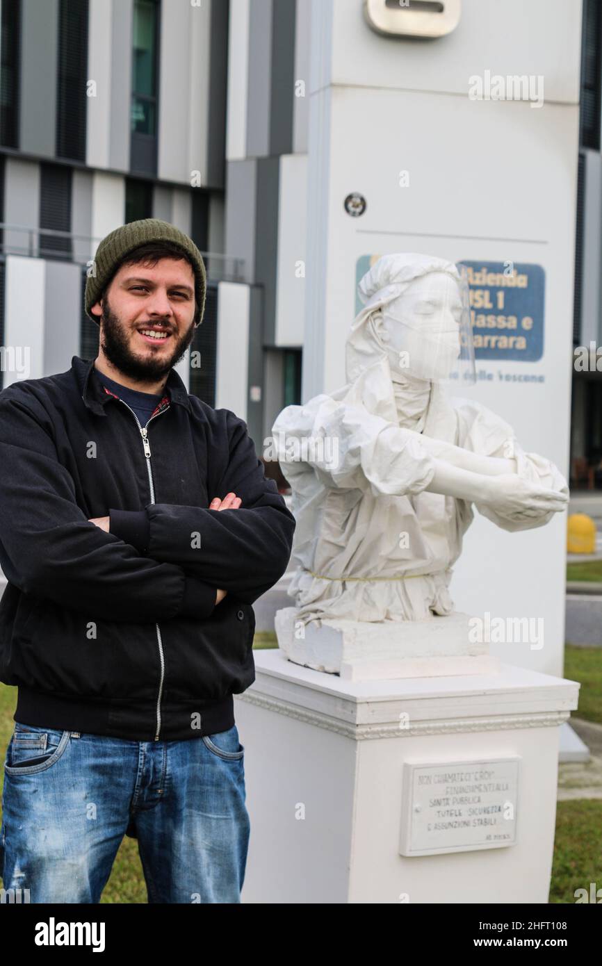 Foto Iacopo Giannini - LaPresse 27-11-2020 Massa Carrara (Ms), Elia Buffa artista emergente e di denuncia, durante la sua quarentana per covid ha realizzato una scultura di denuncia a favore degli operatori sanitari, con la dicitura 'Non Chiamateci Eroi. Finanziamenti alla sanità pubblica'. Al suo attivo Elia oltre a questa scultura è anche l'autore del murales raffigurante 'Maradona e Che Guevara' all'interno del campo da calcio dell'ex OPG di Napoli . Nella foto: L'artista Elia Buffa all'esterno dell'Ospedale Noa di Massa con la sua scultura Stock Photo