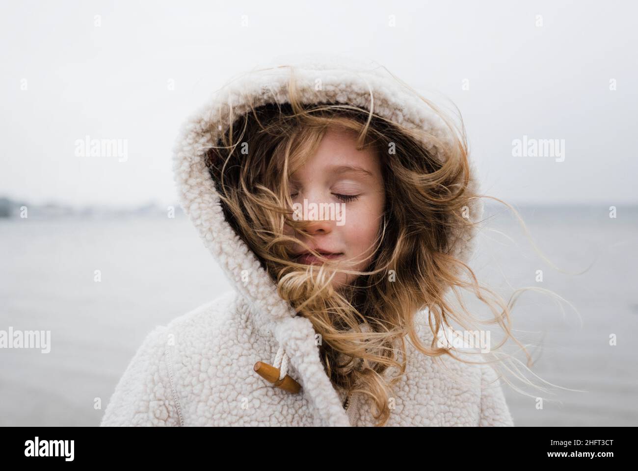 girl stood outside relaxing with her eyes closed at a windy beach Stock Photo