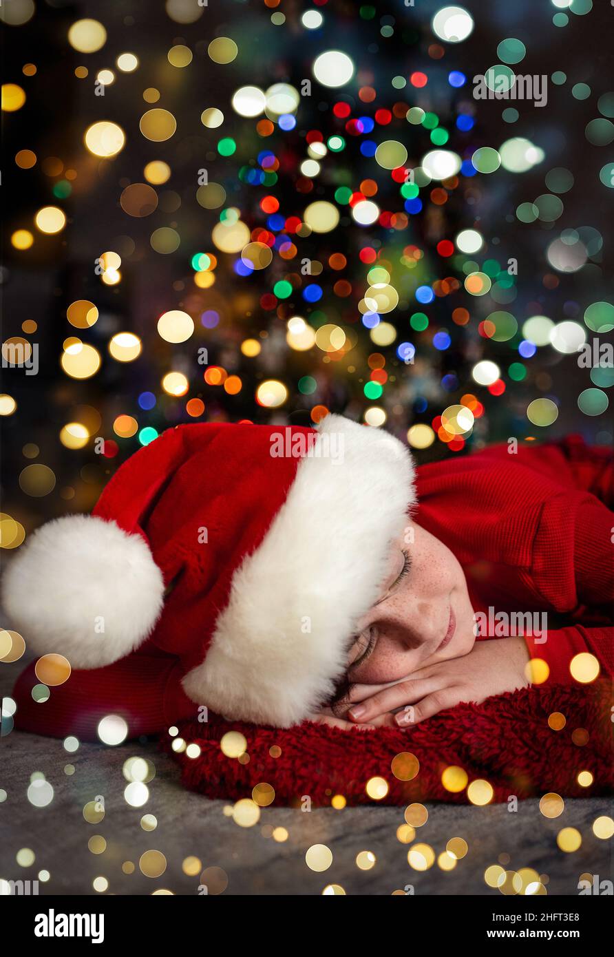 Portrait of boy wearing Santa hat sleeping in front of christmas tree. Stock Photo