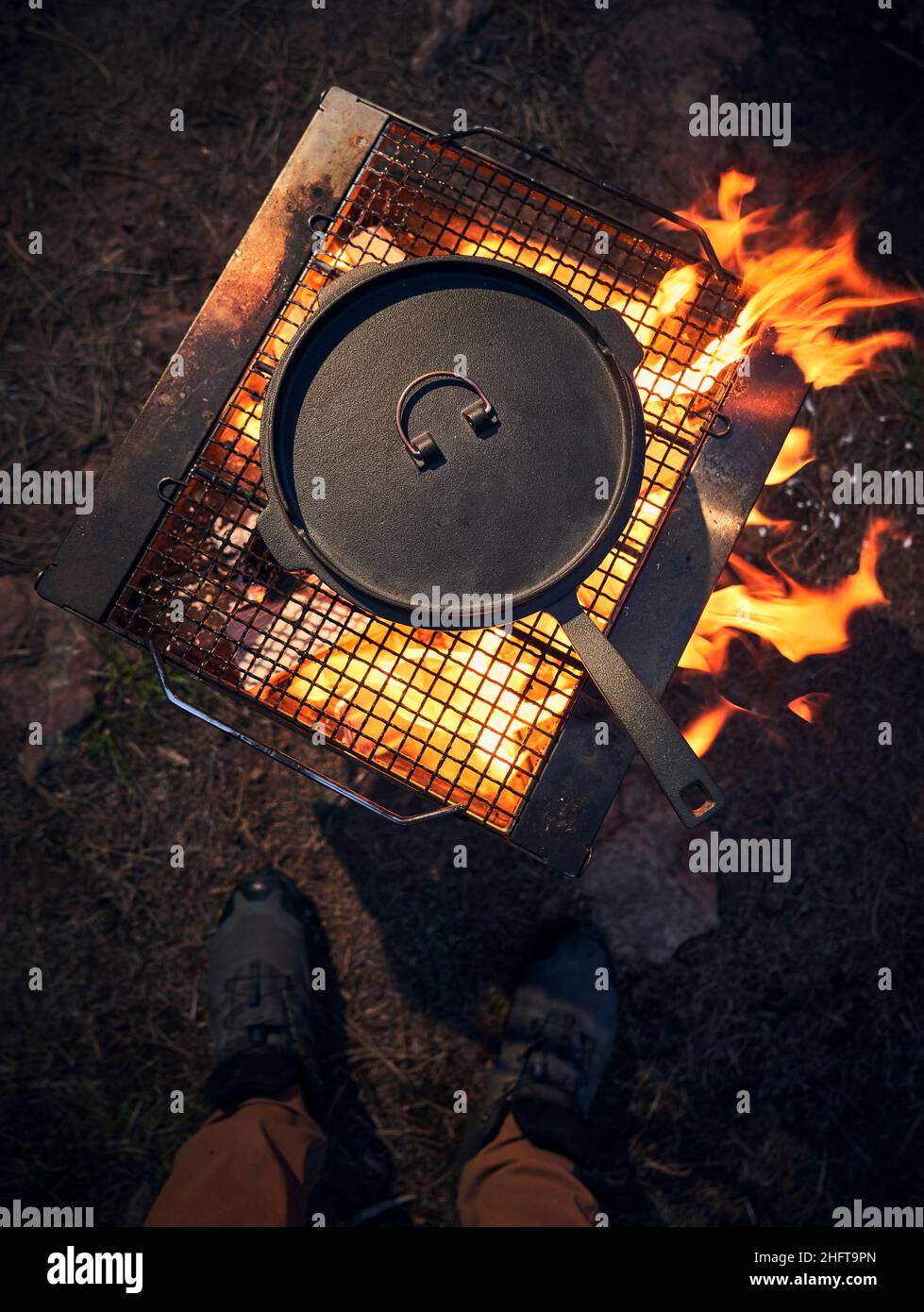 Man stands over a cast iron cooking over an open fire. Stock Photo