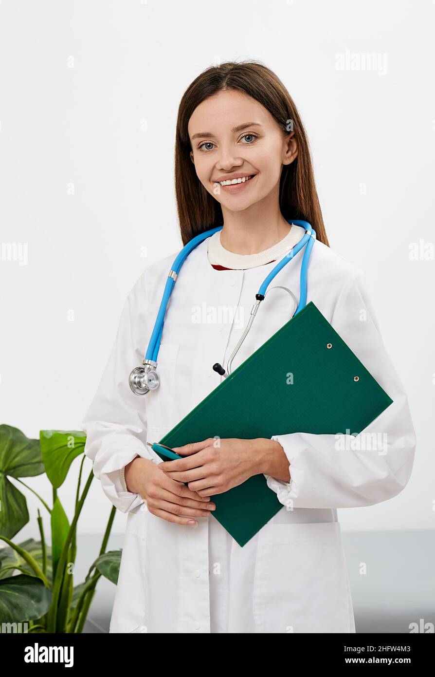 doctor occupation. Brunette female general practitioner with patient's medical record in her hands standing in a medical clinic, portrait Stock Photo