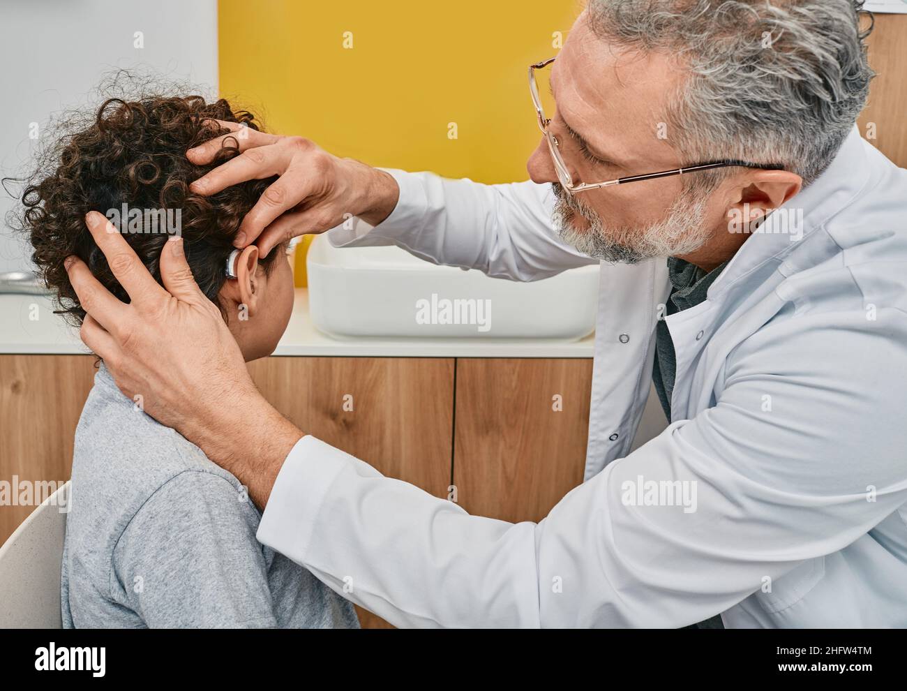 Audiologist putting a hearing aid on male child ear while visit hearing clinic. Hearing solutions Stock Photo
