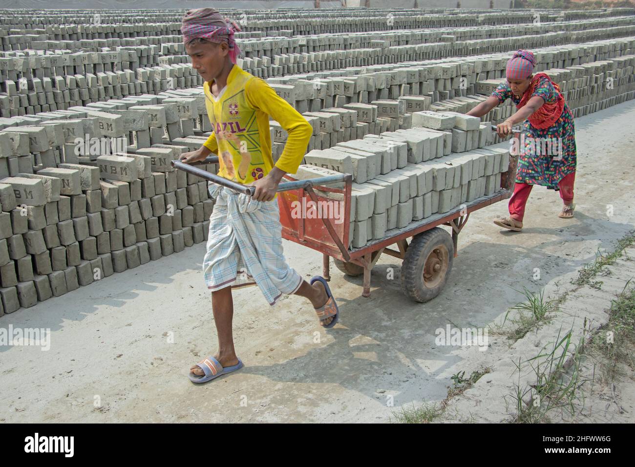 Narayanganj, Dhaka, Bangladesh. 18th Jan, 2022. Workers are carrying bricks on a trolly in a brick field in Narayanganj, Bangladesh. Bangladesh, with its 160 million inhabitants, is a country in constant demand for bricks as the primary material for construction of buildings in the era of urbanization. There are approximately 5000 privately operated brick kilns within Bangladesh, including 1000 around the capital, Dhaka. Brick kilns, indirectly responsible for climate change, emit toxic fumes containing large amounts of carbon monoxide, nitrogen oxide and oxides of Sulphur which are extremel Stock Photo