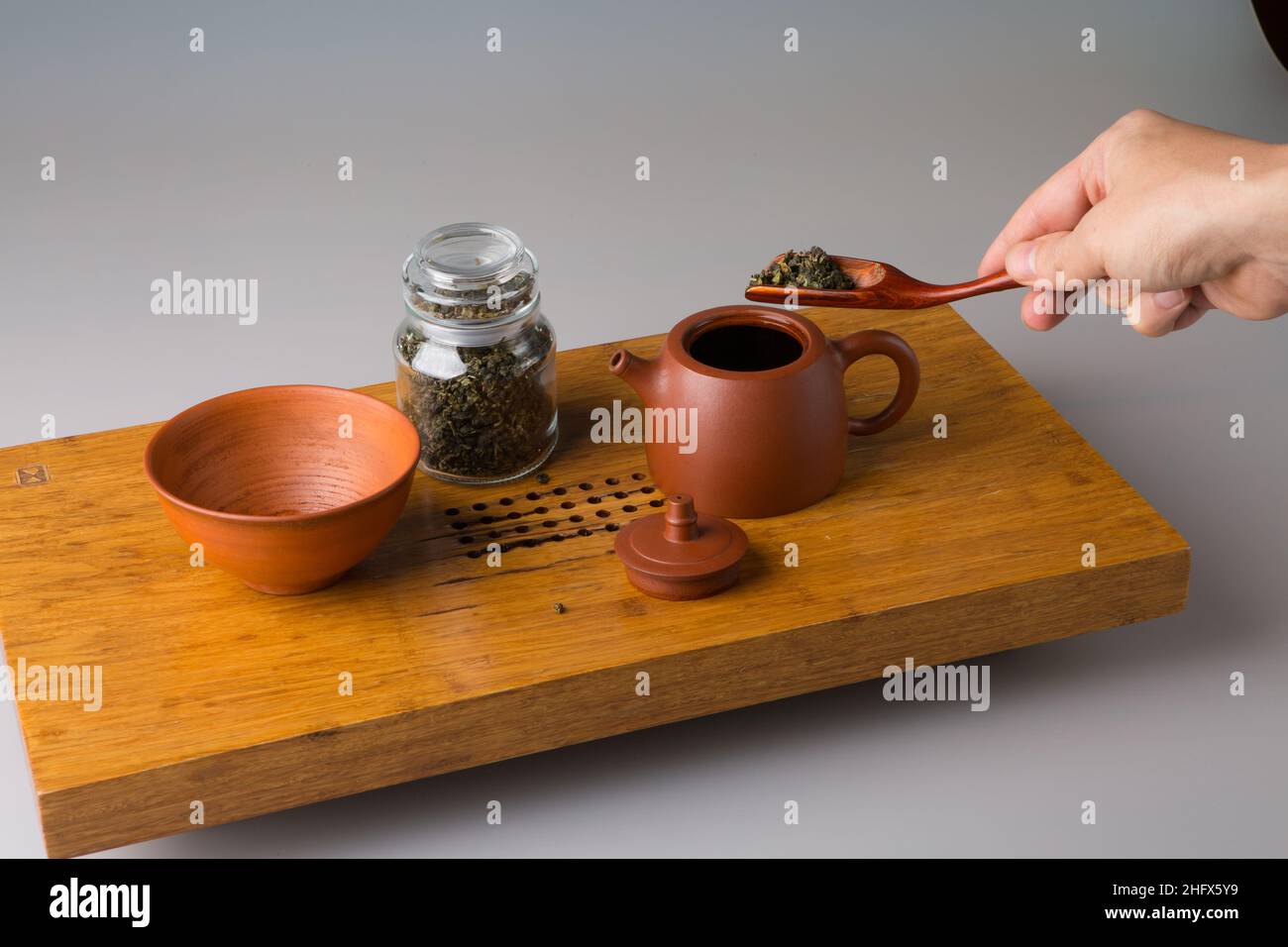 A man's hand puts oolong green tea into a clay teapot. A cup on a table