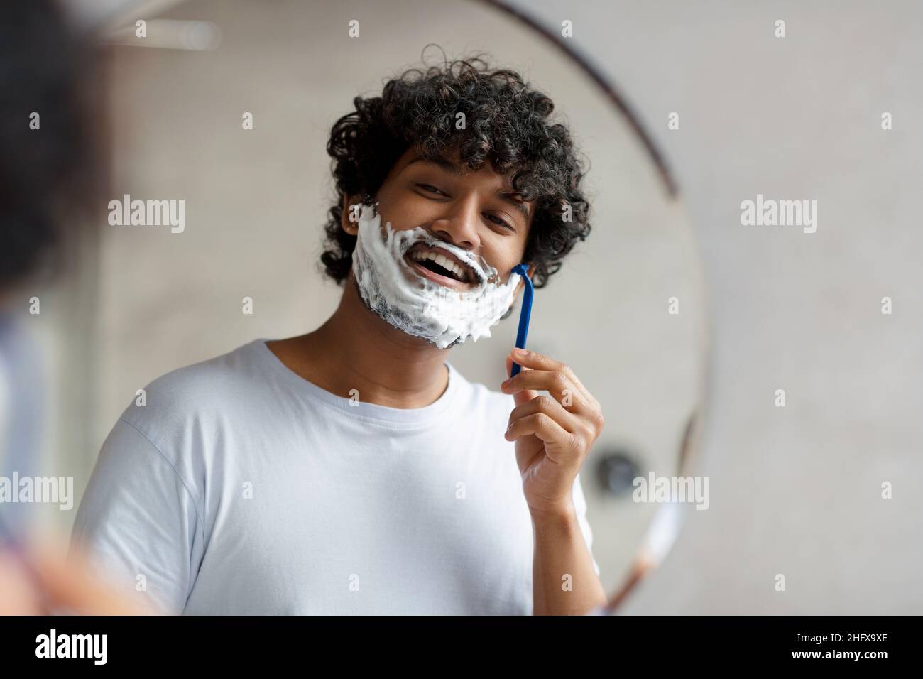 Portrait of indian man shaving near mirror in bathroom, guy with shave