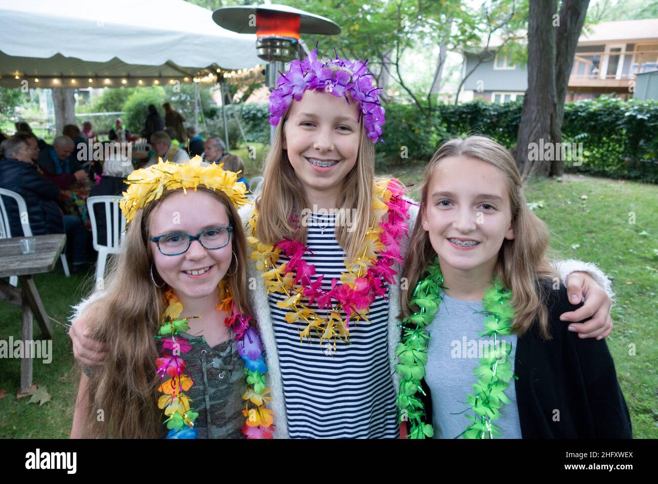 Three cousins wearing colorful leis posing and enjoying grandparent's anniversary party held in their backyard. Minneapolis Minnesota MN USA Stock Photo