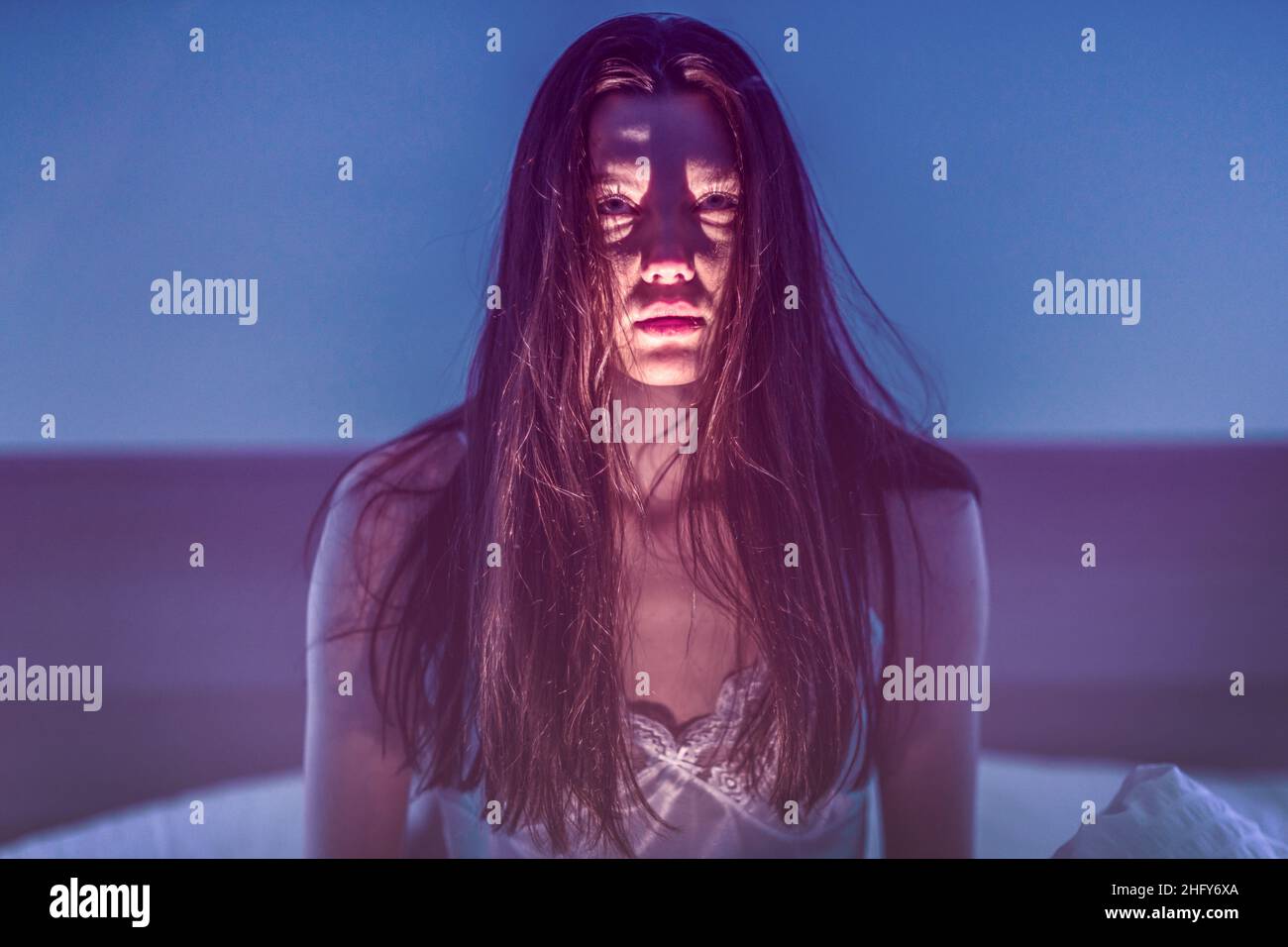Scare. Horror. Scary girl with dark hair. The woman shines a flashlight at herself from below and creates a scary face. Stock Photo