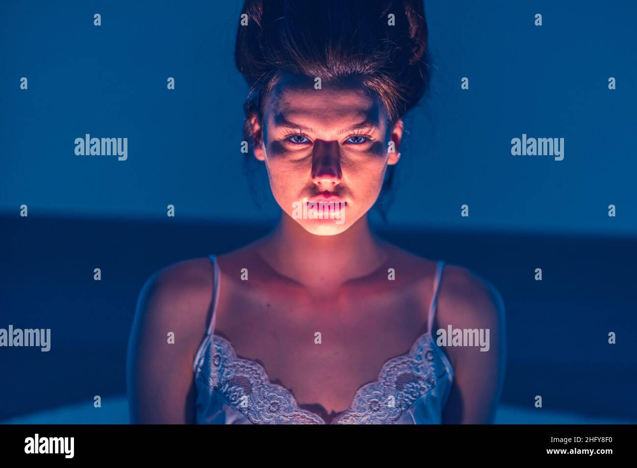 Horror. The woman shines a flashlight at herself from below and creates a scary face. Scary girl with dark hair. Scare. Stock Photo