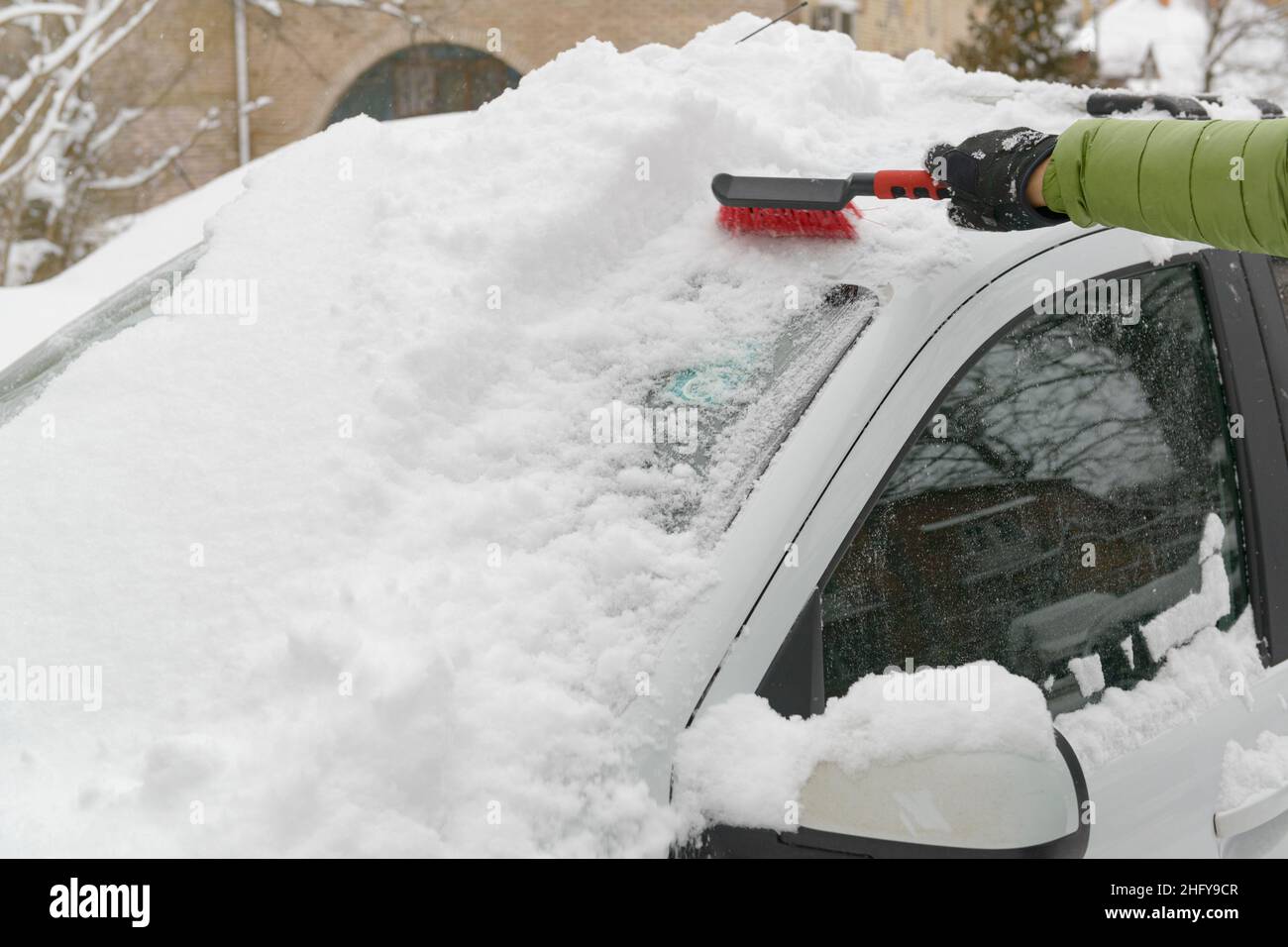 A car owner removing snow of his car in winter Stock Photo