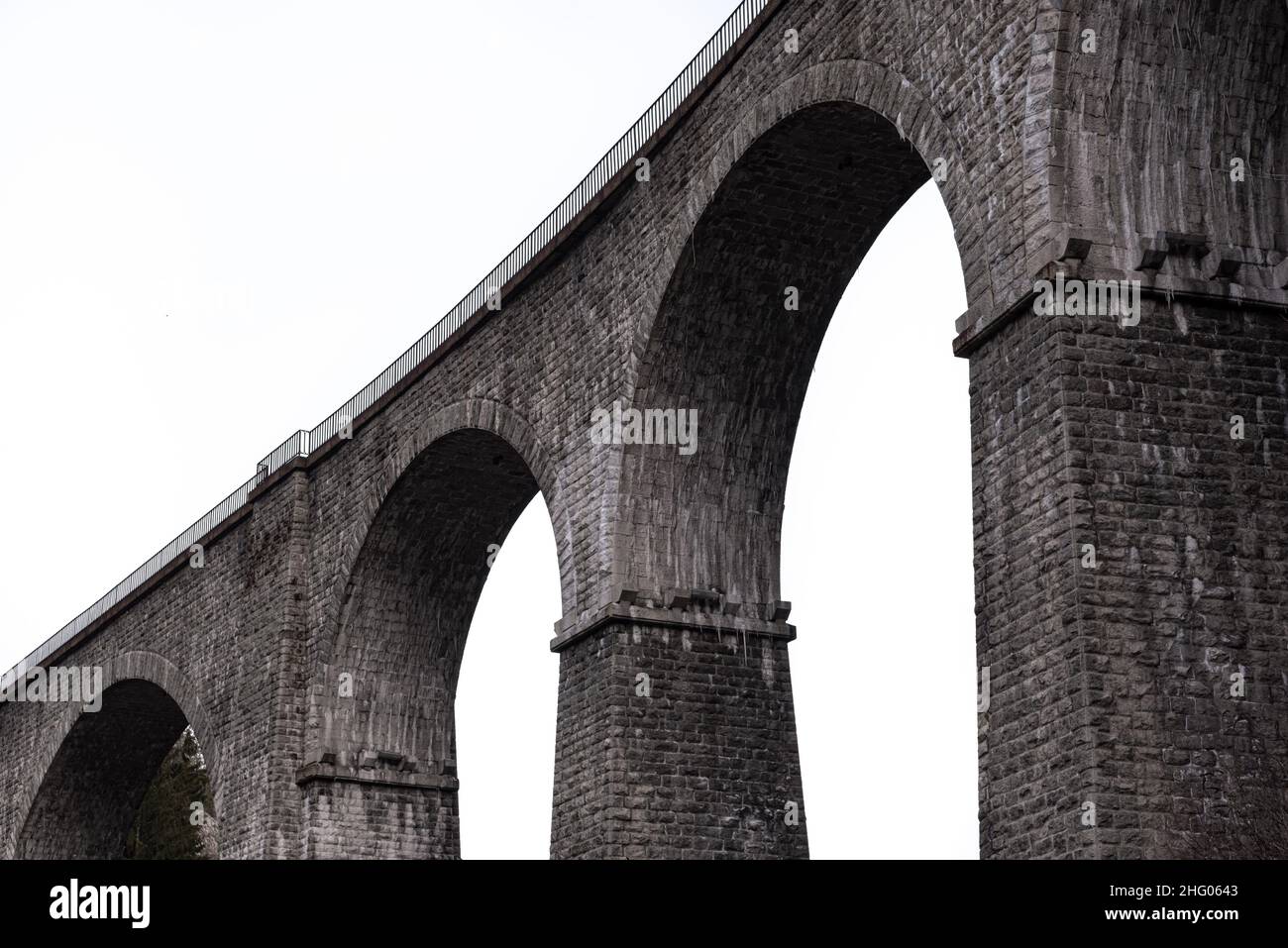 Architectural detail in close-up view from below of arches and columns pillars of stone brick railway bridge against high key lighting sky in Chamonix Stock Photo