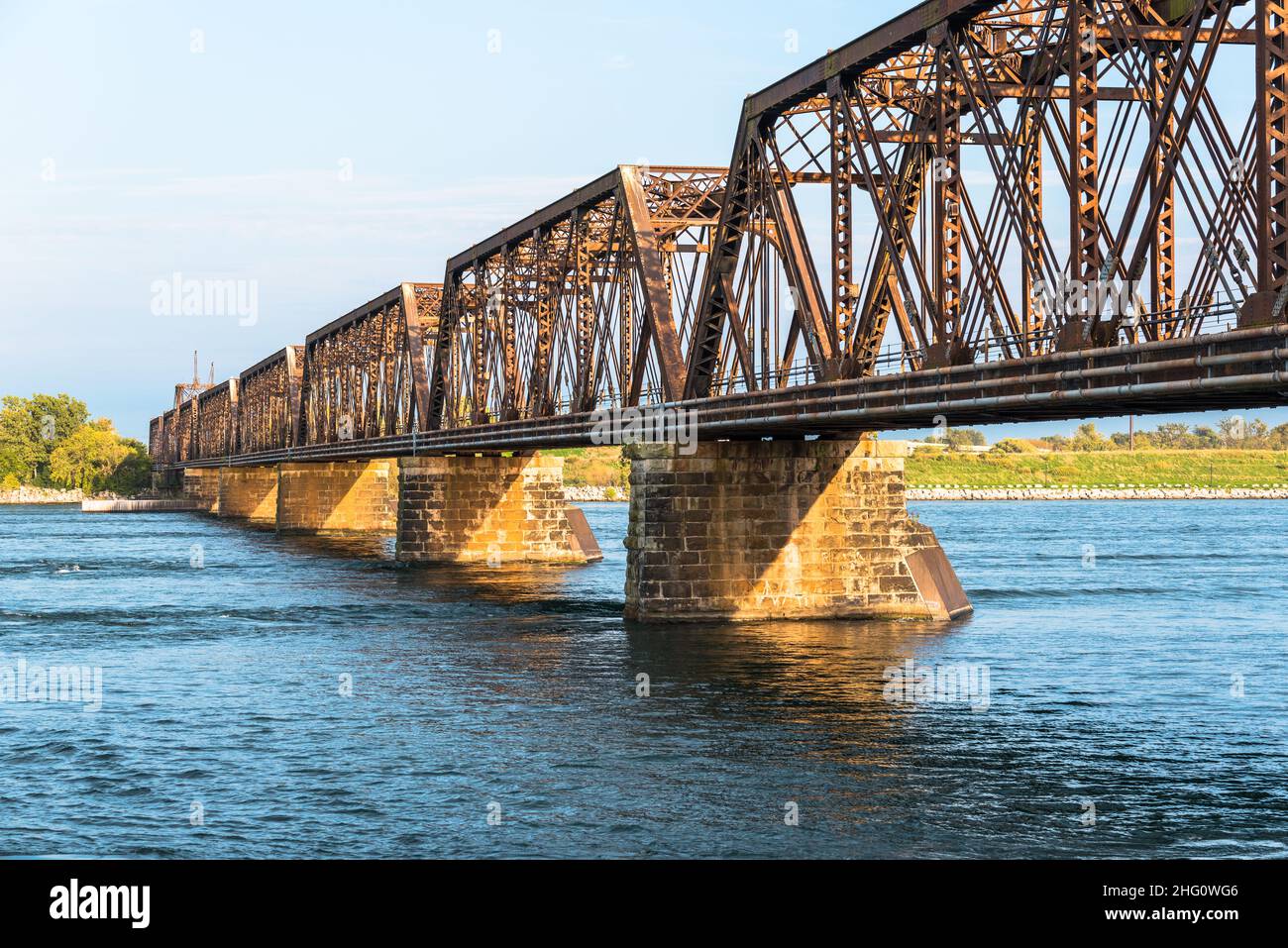 View of an empty rusty railroad bridge across a river at sunset Stock Photo