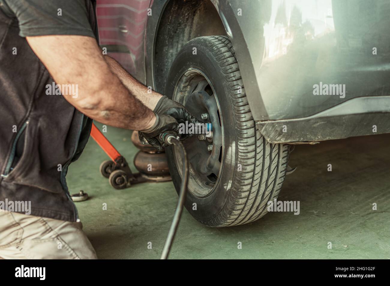 Mechanic using an electric screwdriver to remove a wheel in a garage Stock Photo