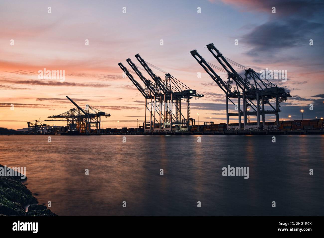 shipping container cranes towering over waterway at port at sunset ...