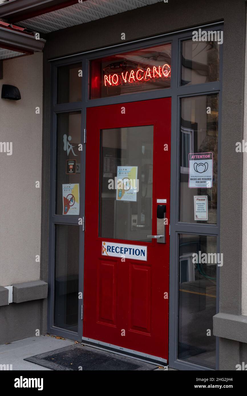 Jasper Alberta Canada, September 27 2021:A NO VACANCY sign illuminated at the door to the town of Jasper Hostel above a red door. Stock Photo