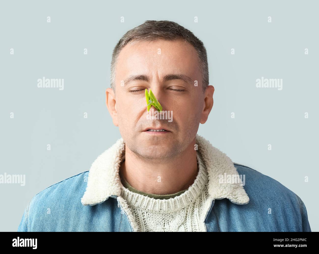 Ill mature man with clothespin on his nose against grey background