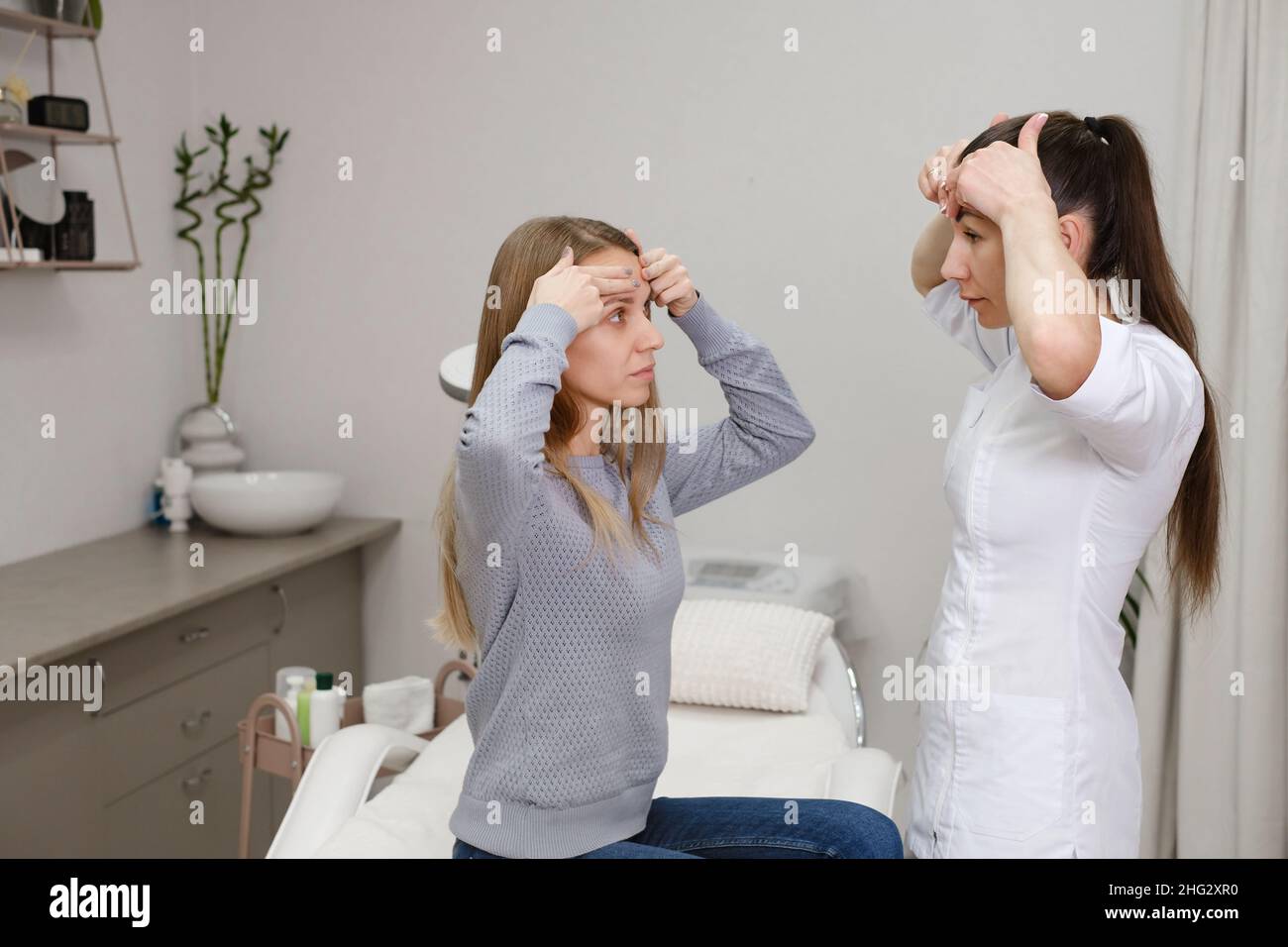 Client woman doing massage with dermatology cosmetician specialist in clinic, discussion skin face problems. Woman showing zones for treatment Stock Photo
