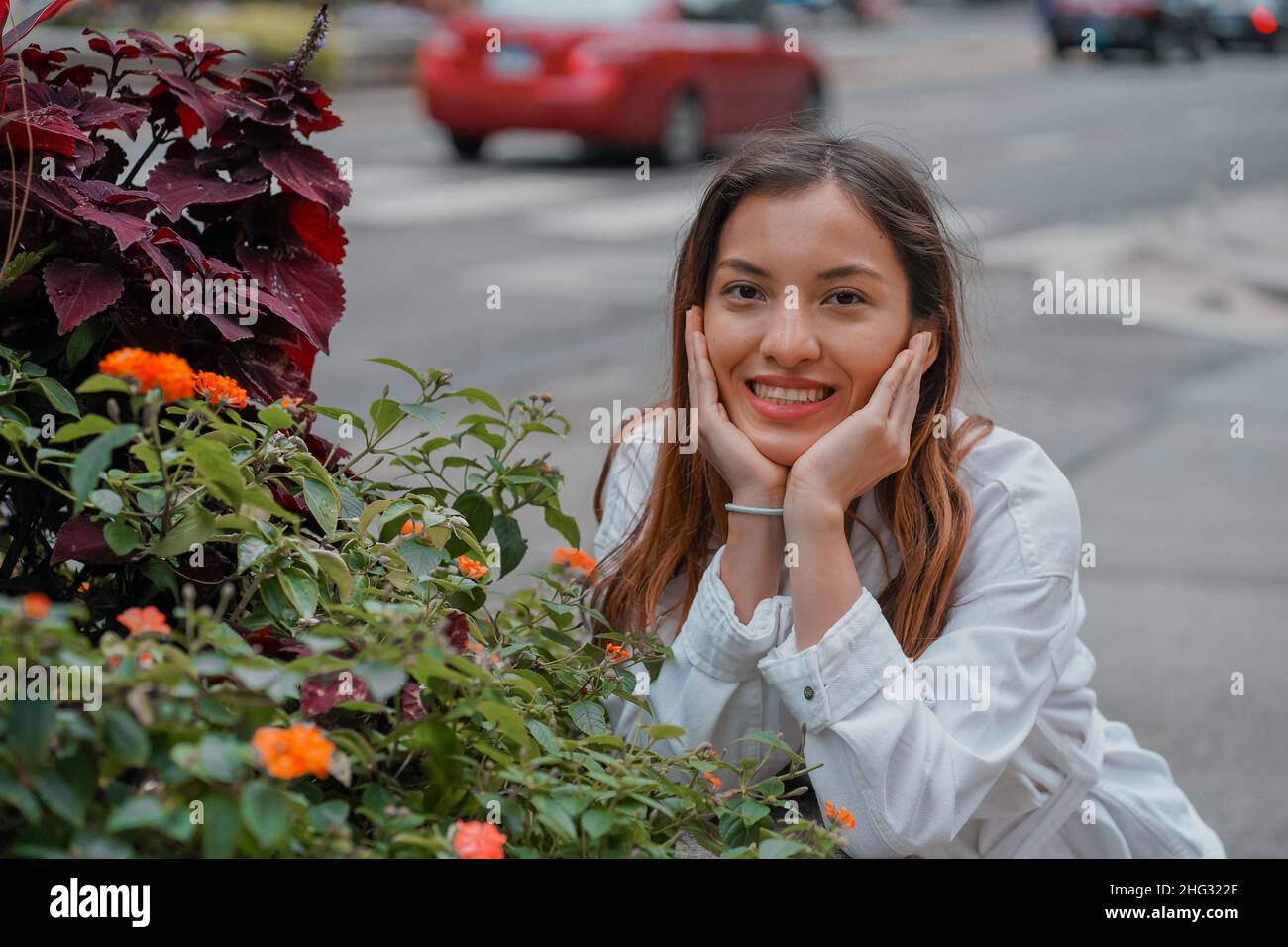 Shallow focus of a pretty happy smiling Caucasian female with a grace face next to flowers outdoors Stock Photo