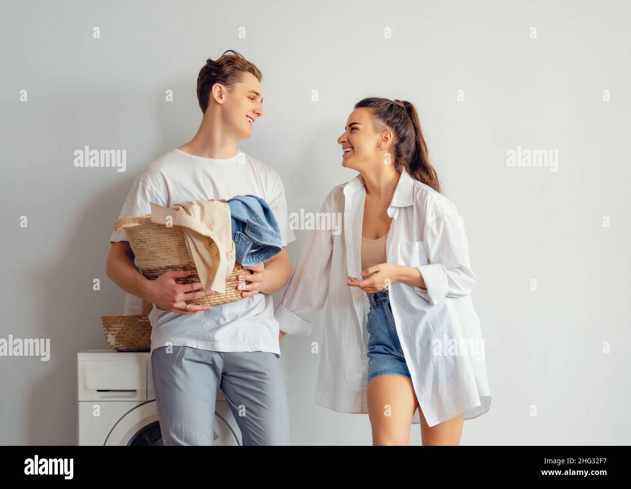 Beautiful young loving couple is smiling while doing laundry at home ...
