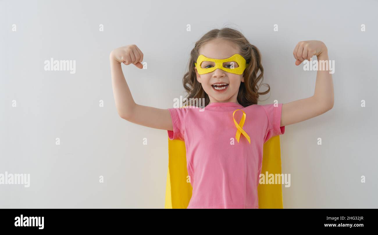 World Childhood cancer Day.  Girl in superhero costume with golden ribbon. Stock Photo