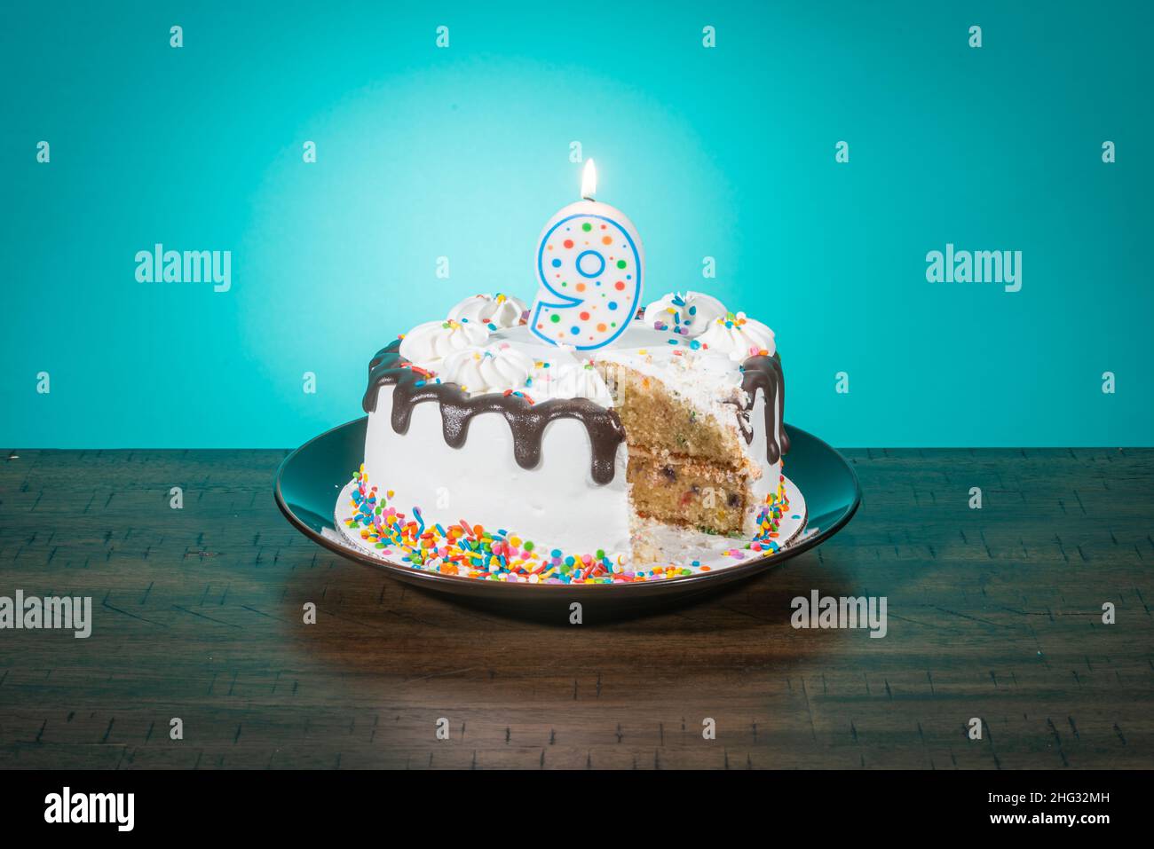 A birthday cake, missing a slice, bears a candle in the shape of the number 9. Stock Photo