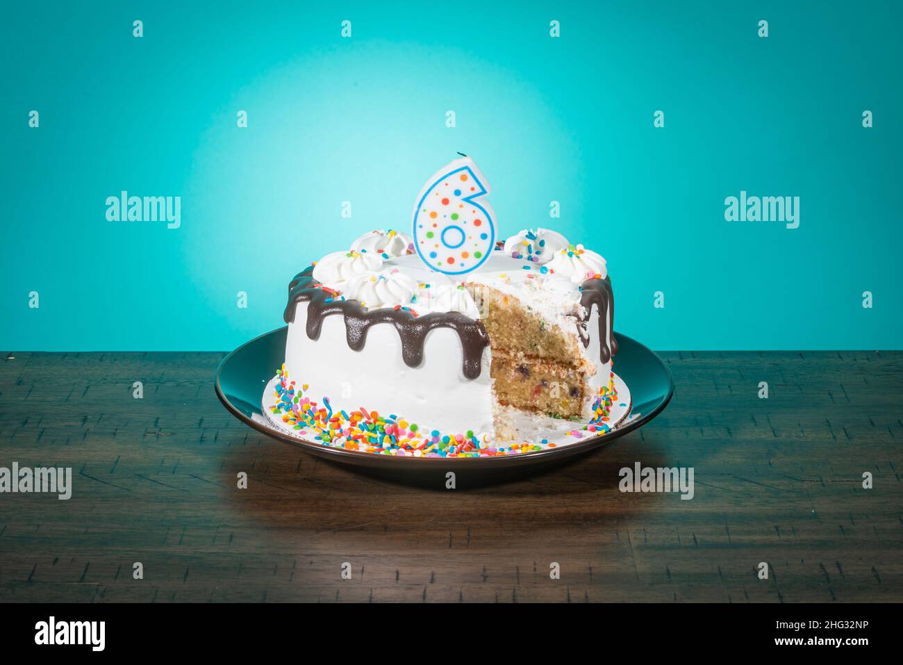 A birthday cake, missing a slice, bears a candle in the shape of the number 6. Stock Photo