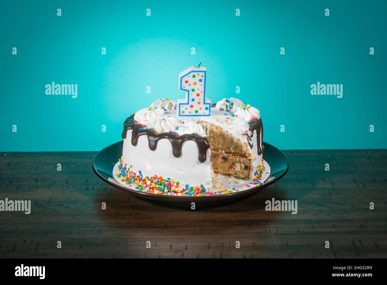 A birthday cake, missing a slice, bears a candle in the shape of the number 1. Stock Photo