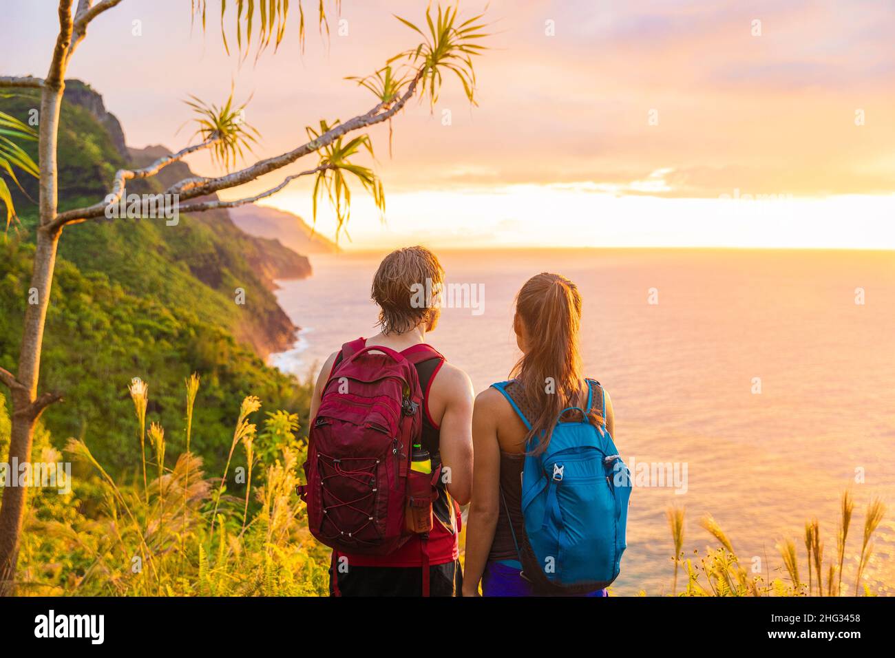 Hawaii hiking hikers hiking on Kalalau trail watching sunset from Na Pali Coast. Tourists couple with backpacks walking outdoor in Kauai island Stock Photo