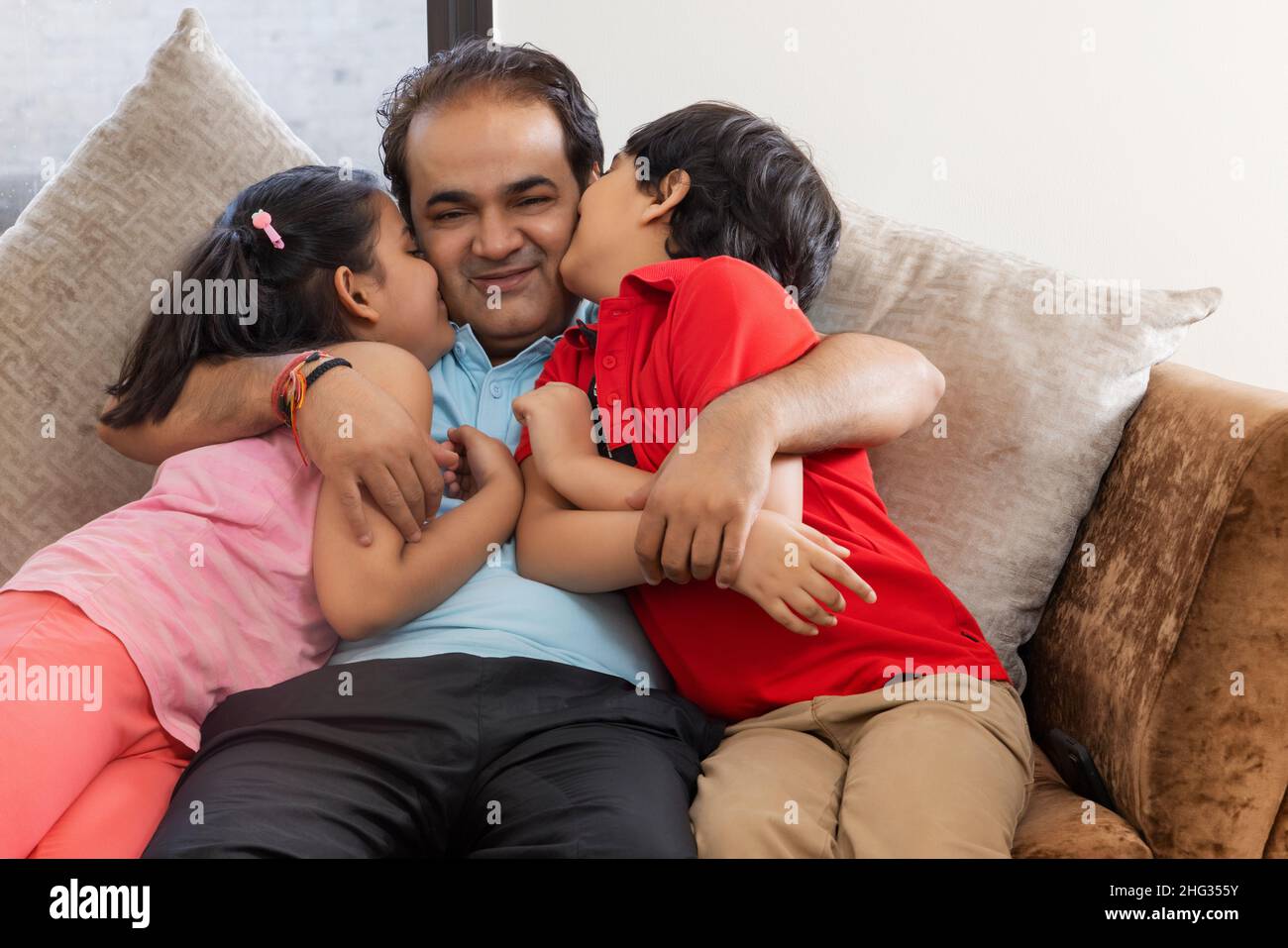 Son and daughter kissing their father together while sitting on sofa Stock Photo