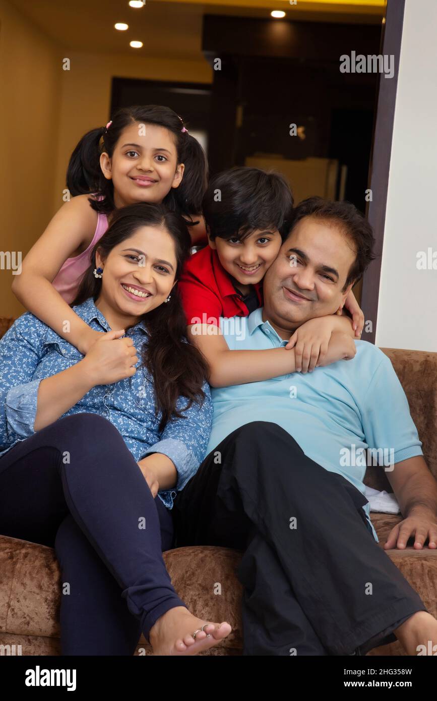 Indian family members posing together in front of camera while sitting on sofa Stock Photo