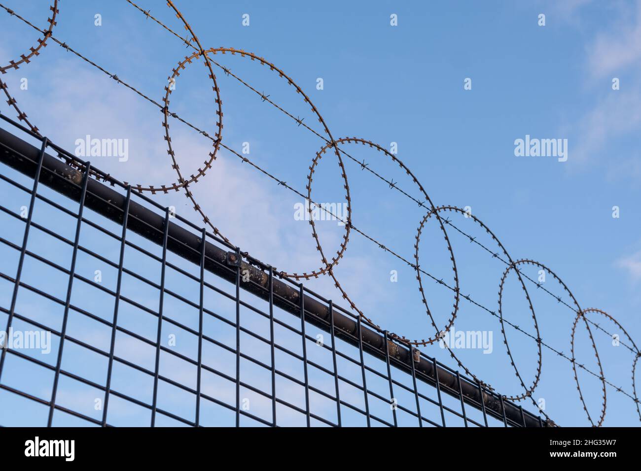 Looking up at circular barbed wire fence against blue sky diagonal juxtaposition Stock Photo
