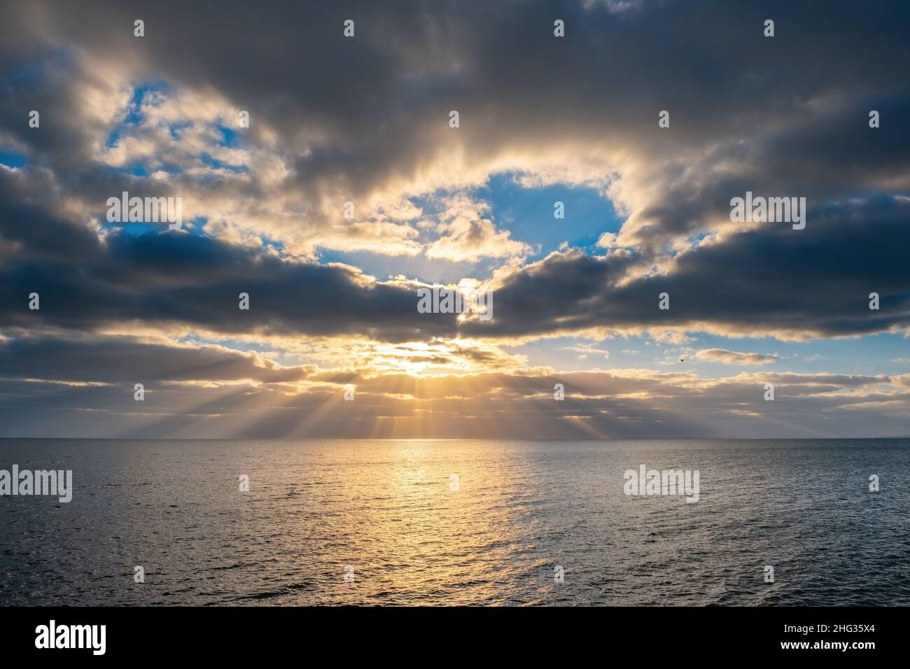 Minimalist seascape at sunset with sun rays protruding through clouds Stock Photo