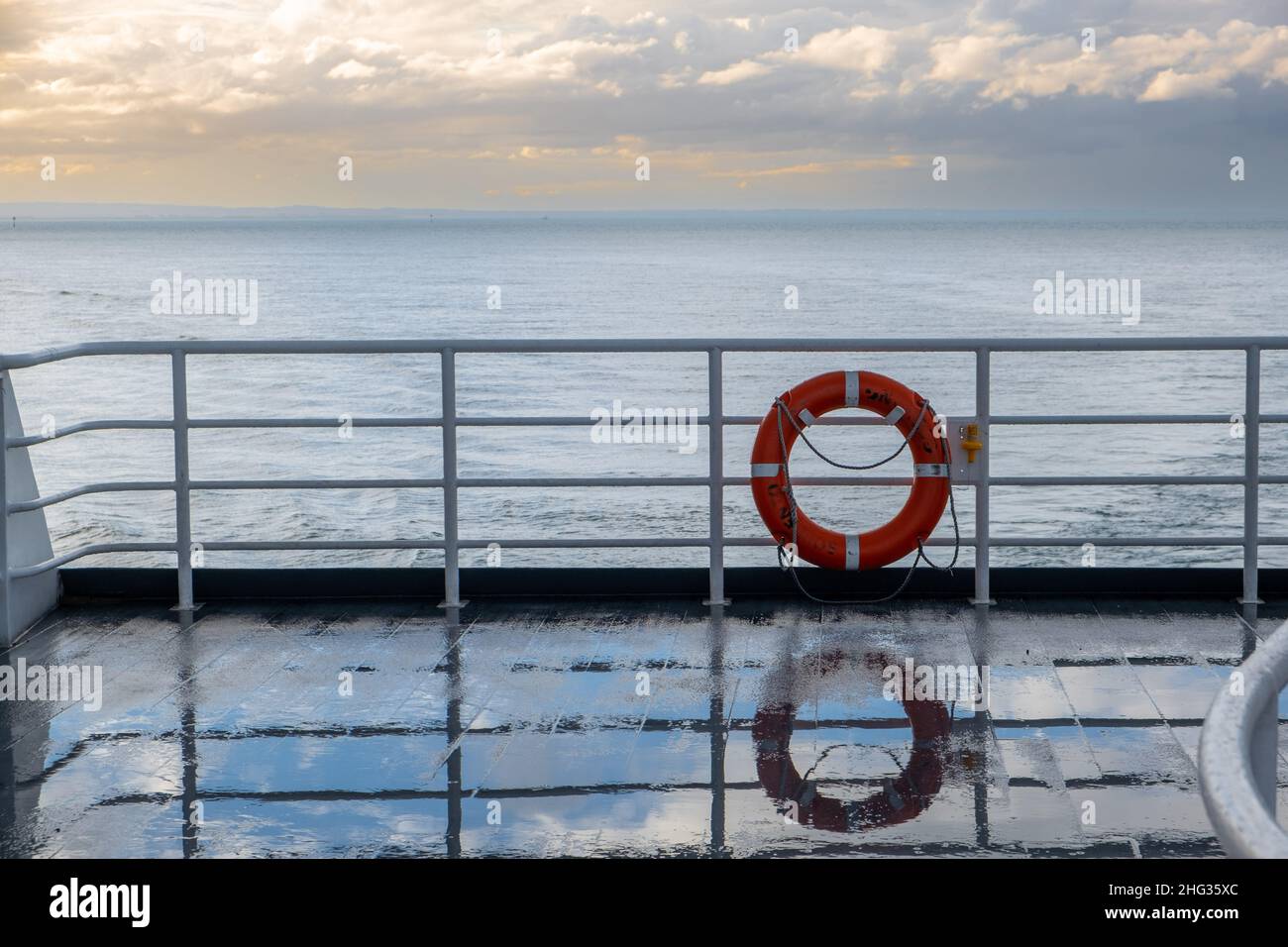 Lifebuoy reflecting in a wet ferry deck at sunset Stock Photo