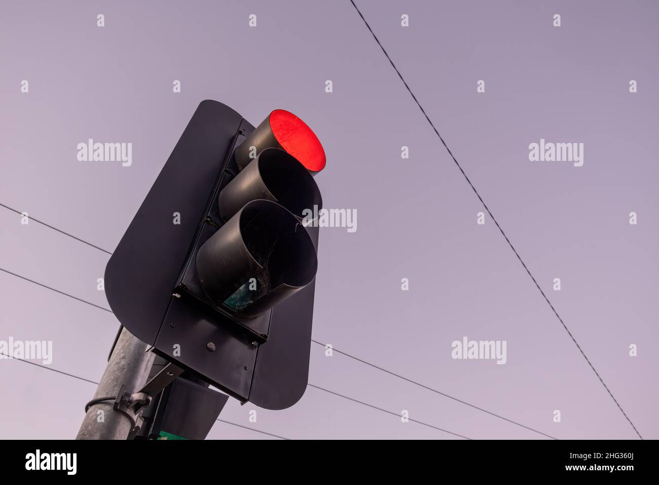 Looking up at red traffic light against the sky at sunset with copy space Stock Photo
