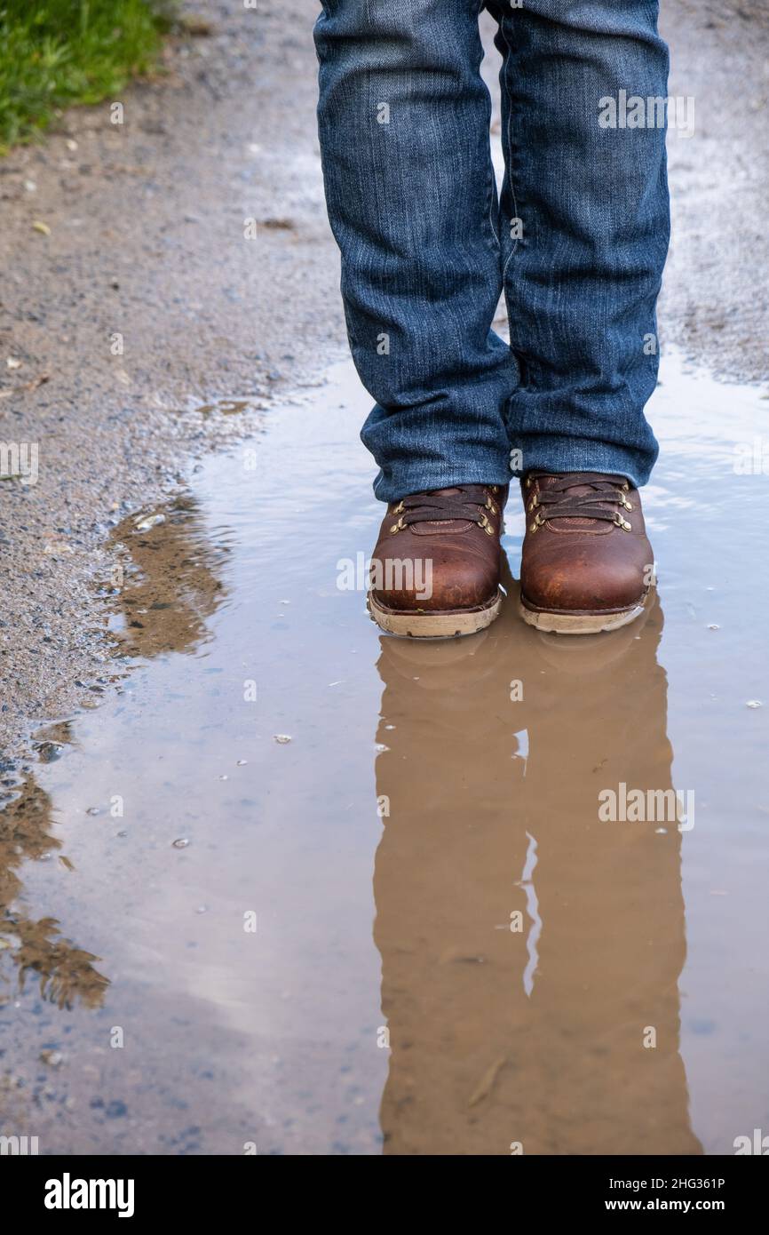 Female feet in hiking boots standing the a puddle with reflections Stock Photo