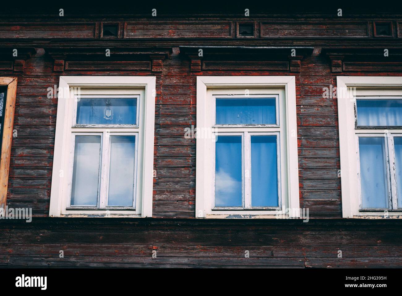 The wall of an old wooden house with red wooden boards and white windows on a sunny day. Stock Photo