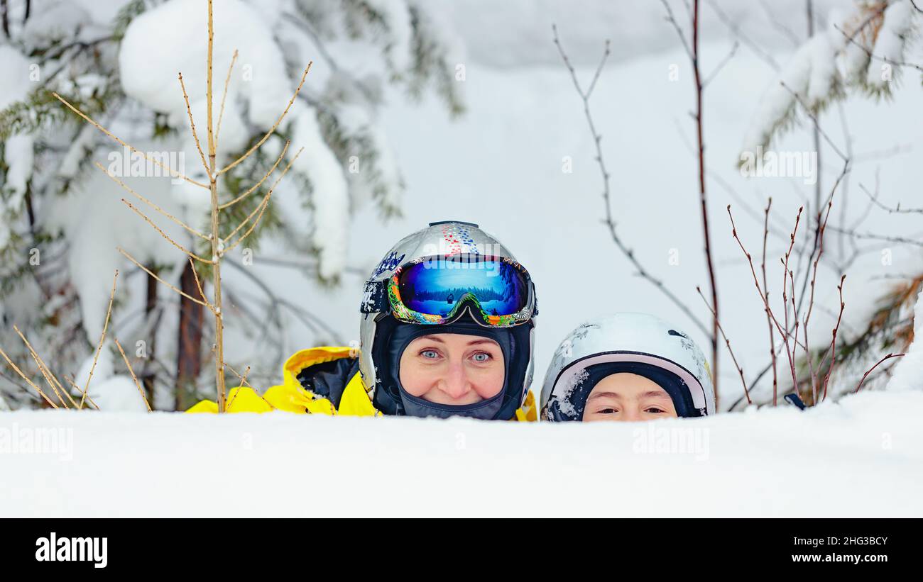 Young women of Caucasian ethnicity and her daughter spend time together in a snowboard park. Mom and daughter in a helmet and goggles Stock Photo