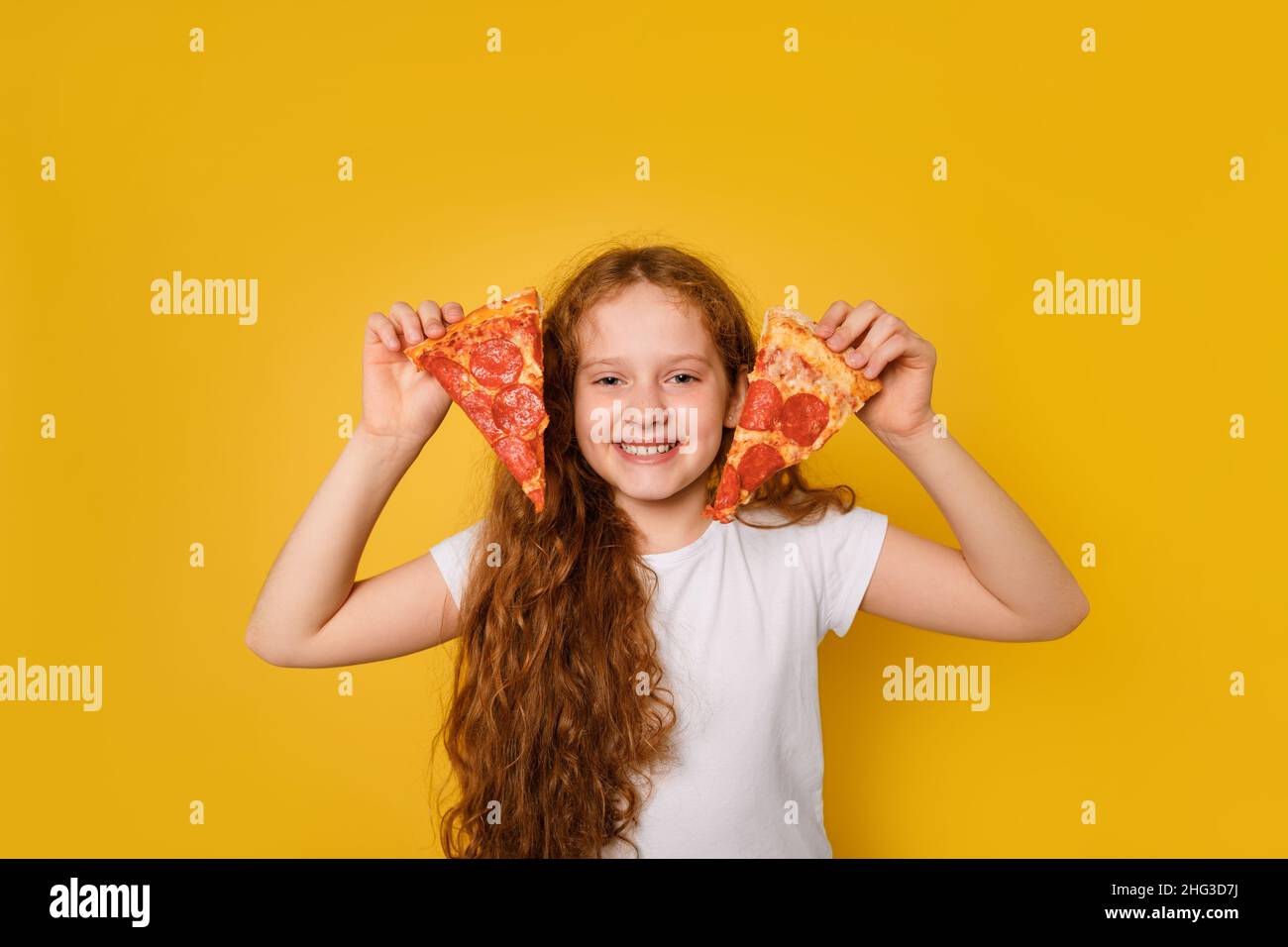 curly girl holds two slices of pizza near her eyes and sticks out her tongue. Stock Photo
