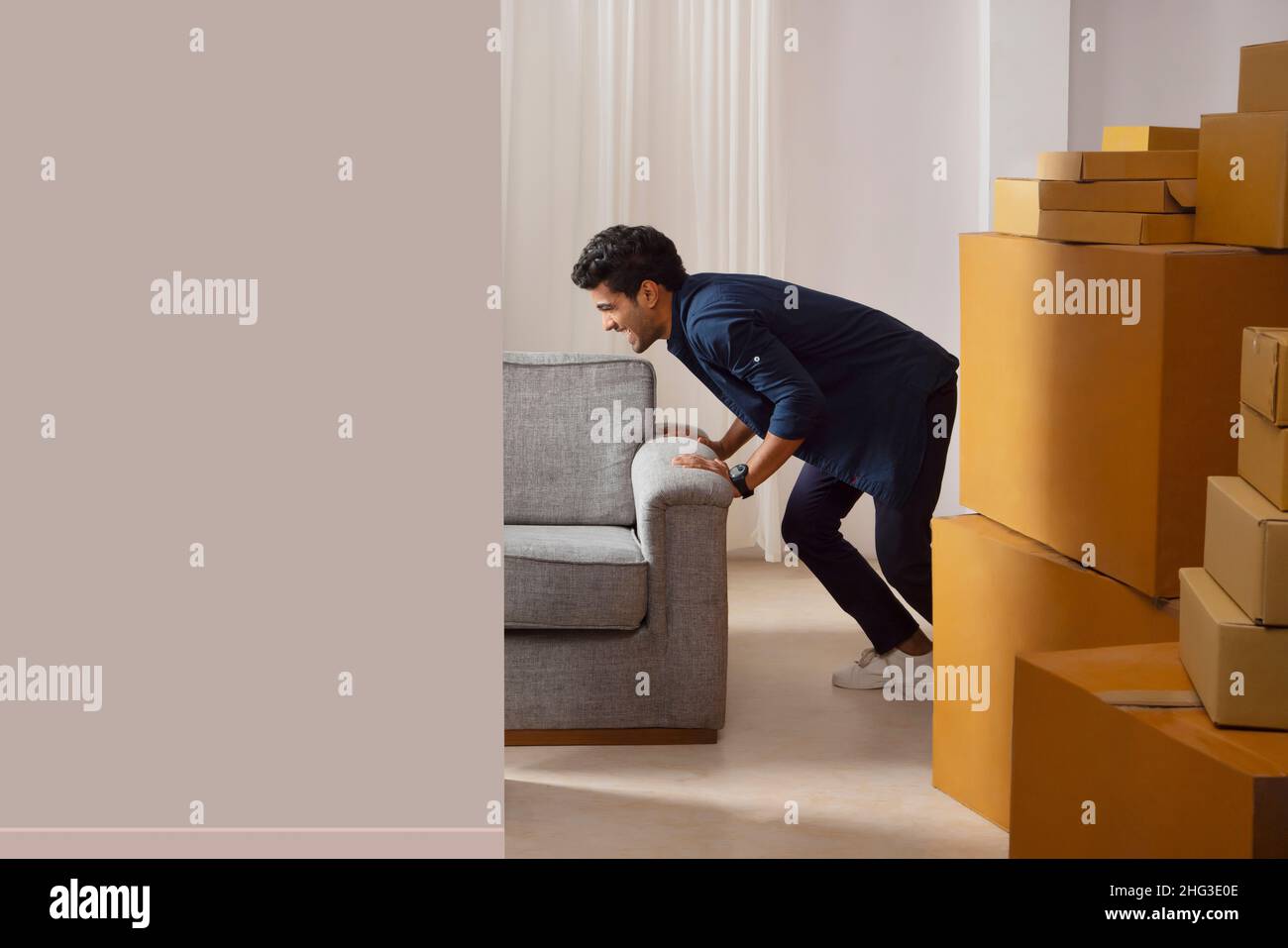 Adult boy alone trying to move sofa Stock Photo