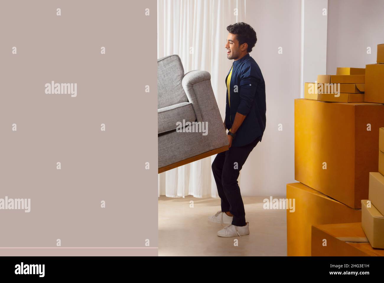 Adult boy lifting sofa and trying to move Stock Photo