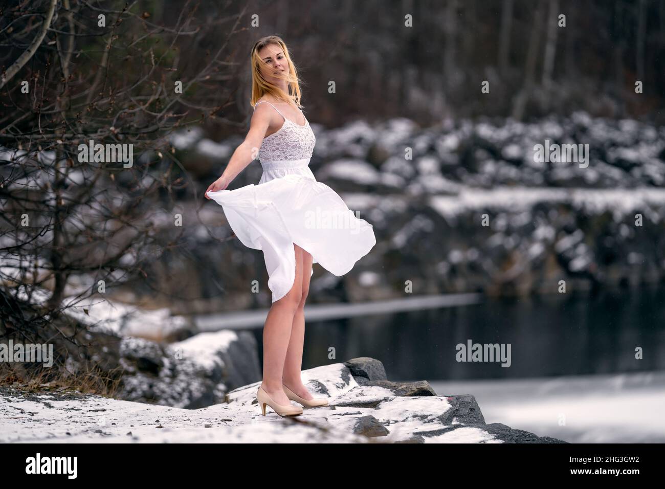 A young woman in a white dress on the shore of a lake in the winter in ...