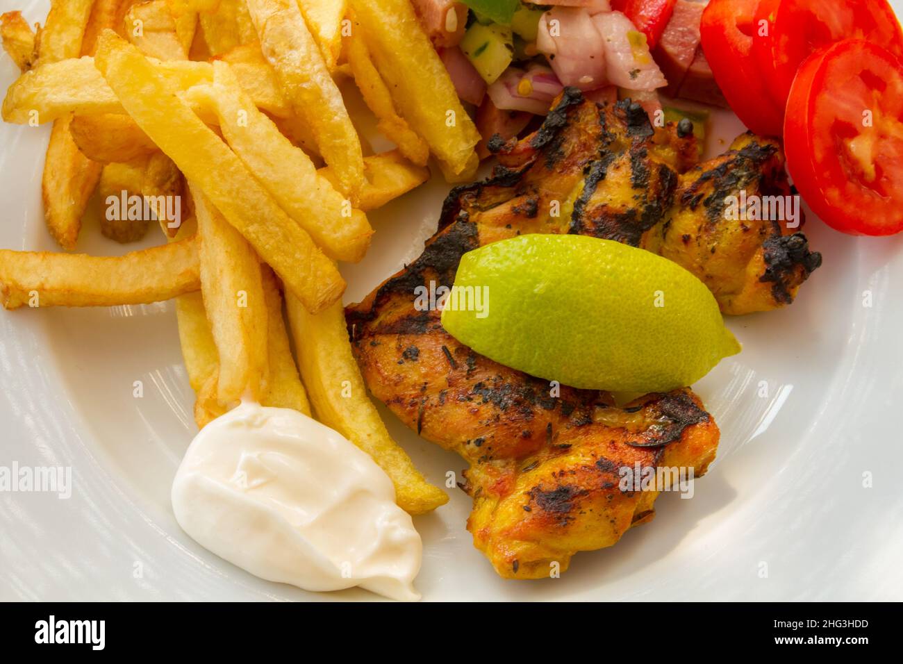 grilled chicken fillet with fries and vegetables in a white plate Stock