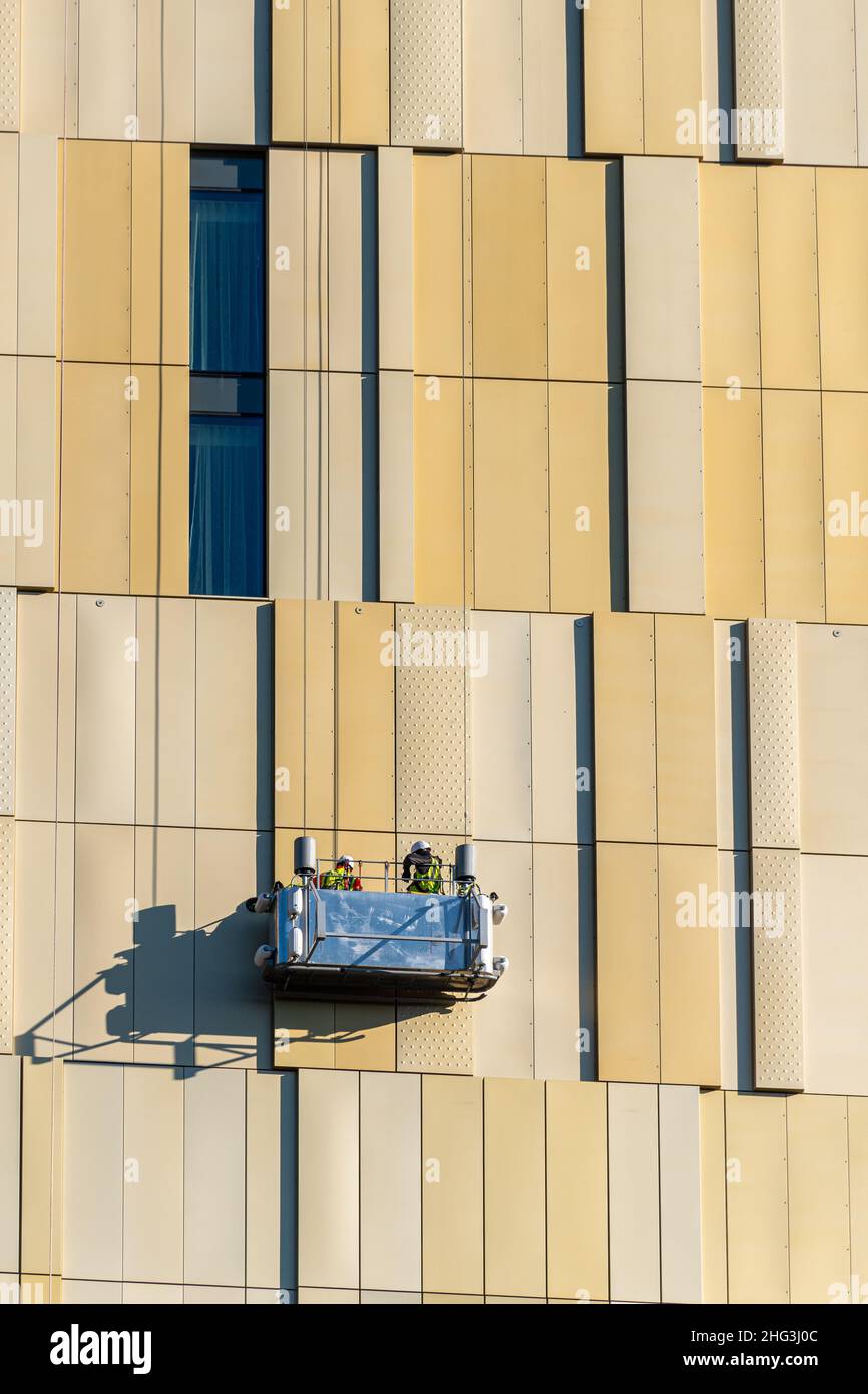 Workers suspended in cradle half-way up the new Hilton Hotel tower block in the Victoria Square Development, Woking town centre, Surrey, England, UK Stock Photo