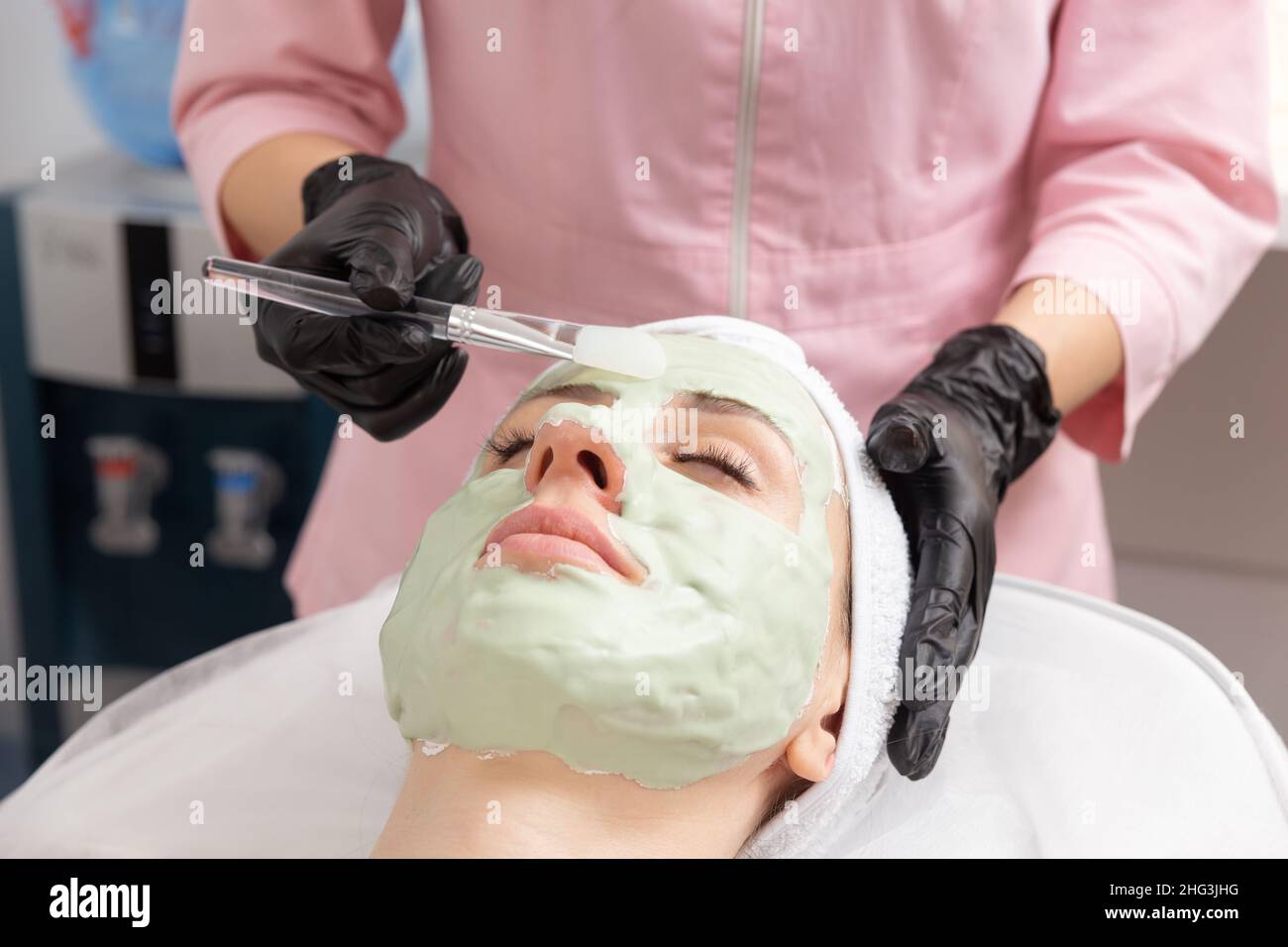 Applying light green facial mask with brush in spa treatment alternative medicine. Face peeling mask, spa beauty treatment, skincare. Stock Photo