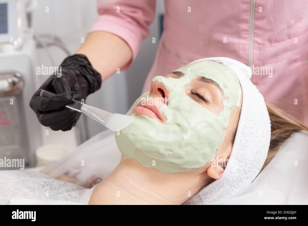 Applying light green facial mask with brush in spa treatment alternative medicine. Face peeling mask, spa beauty treatment, skincare. Stock Photo