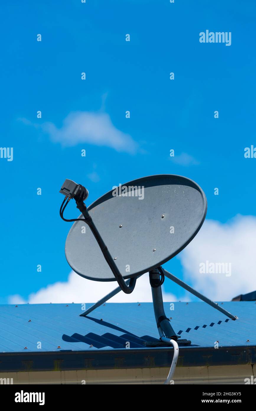 A black satellite dish or receiver or antenna on a hot metal roof with a blue sky background in the Australian sun Stock Photo