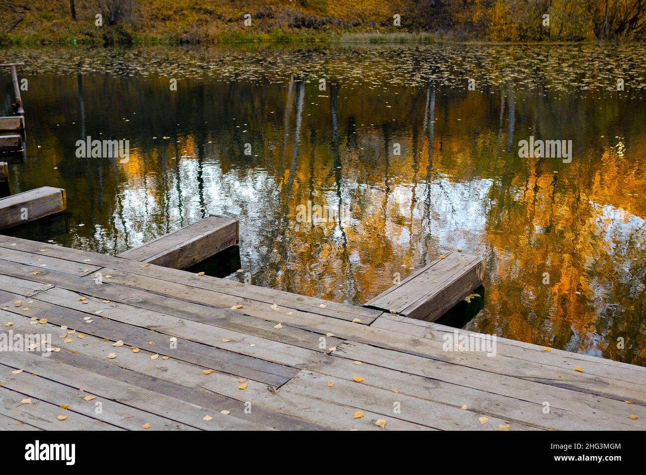 Wooden pier by the lake. Reflection of the autumn forest in the water. No people. Stock Photo